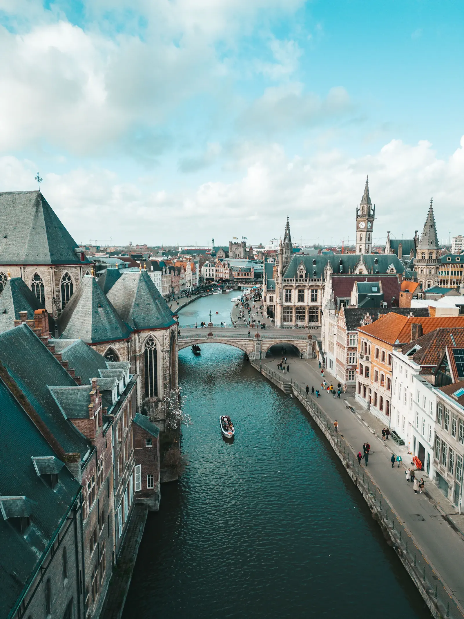 A boat passing under a stone bridge on a canal in Ghent